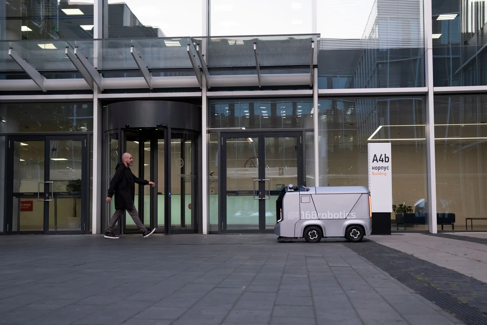 A modern office setting featuring a man and an autonomous delivery robot outside a glass-covered building. Stock photo illustrating L&T Technology Services' product launched story.