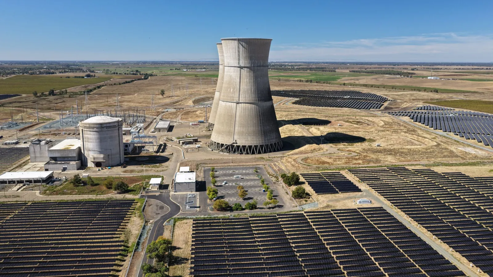 Aerial view of a nuclear cooling tower surrounded by solar panel fields in a rural landscape. Stock photo illustrating Bhageria Industries' production started story.