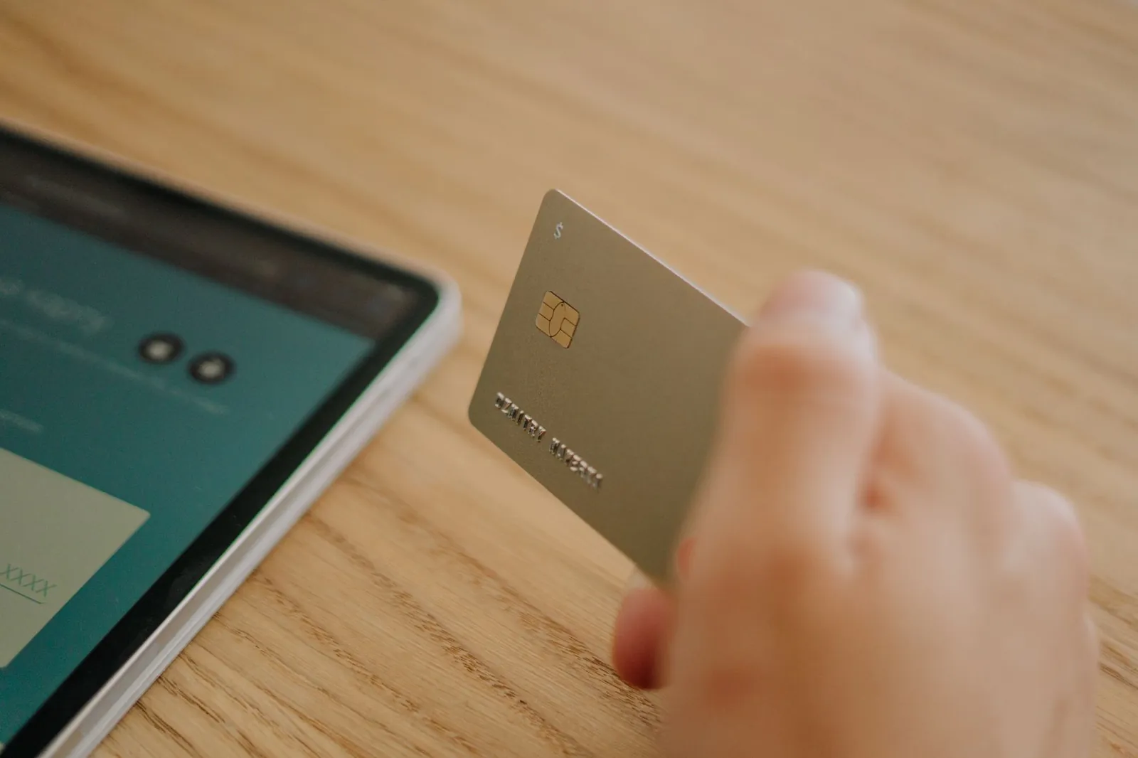 Close-up of a hand holding a credit card near a tablet, depicting online shopping or transaction. Stock photo illustrating Karur Vysya Bank's product launched story.