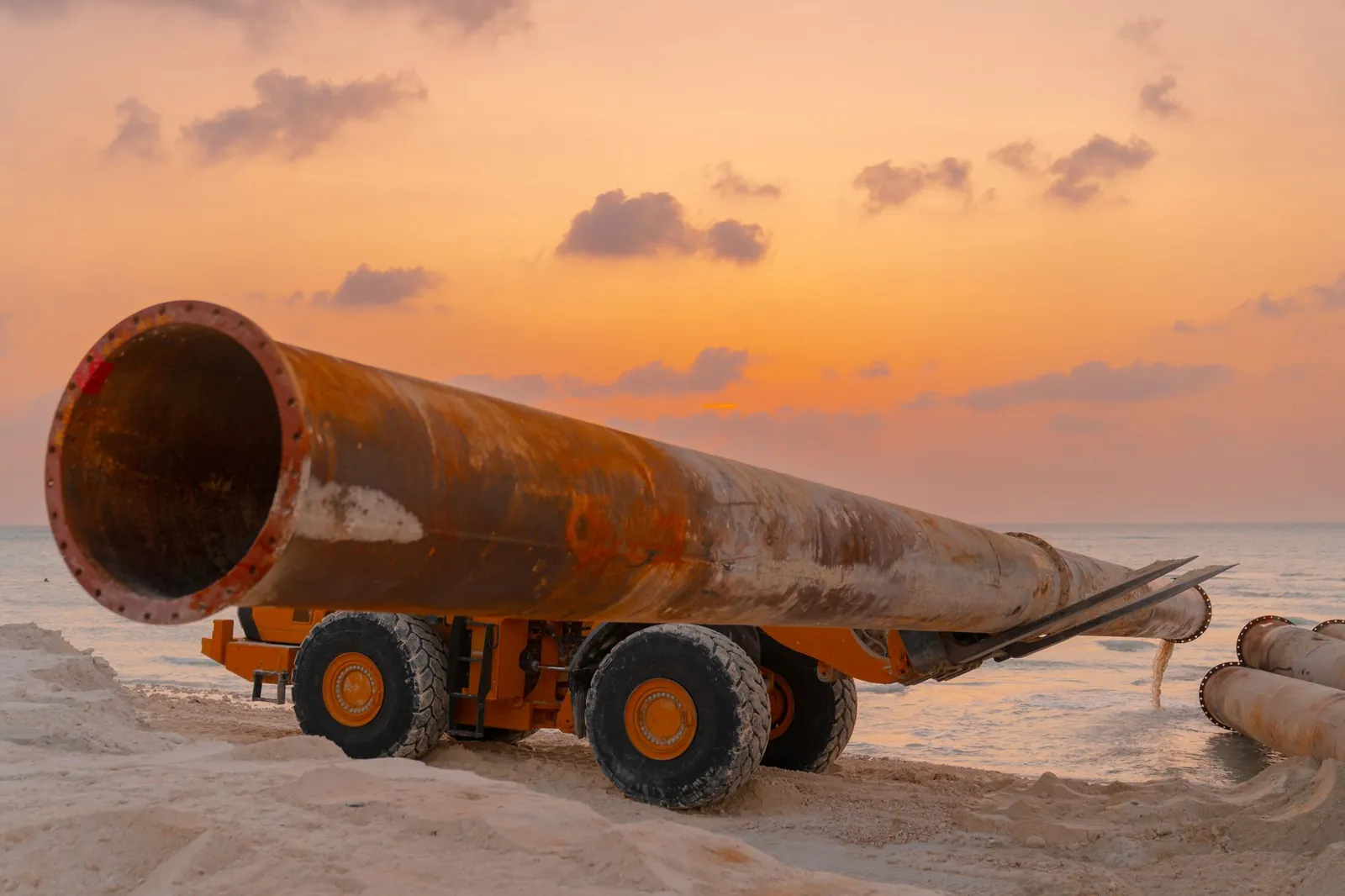 A rusted pipeline and machinery at a coastal construction site during sunset. Stock photo illustrating Kalpataru Projects International's new order story.