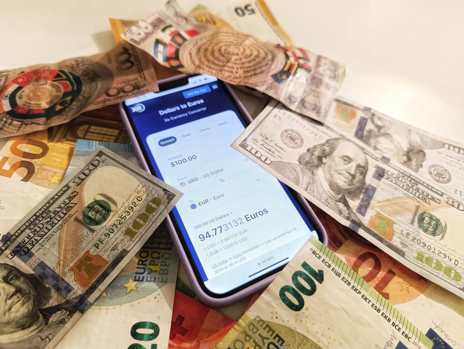 A smartphone displaying a currency converter surrounded by dollar and euro banknotes, highlighting exchange rates. Stock photo illustrating One MobiKwik Systems' product launched story.