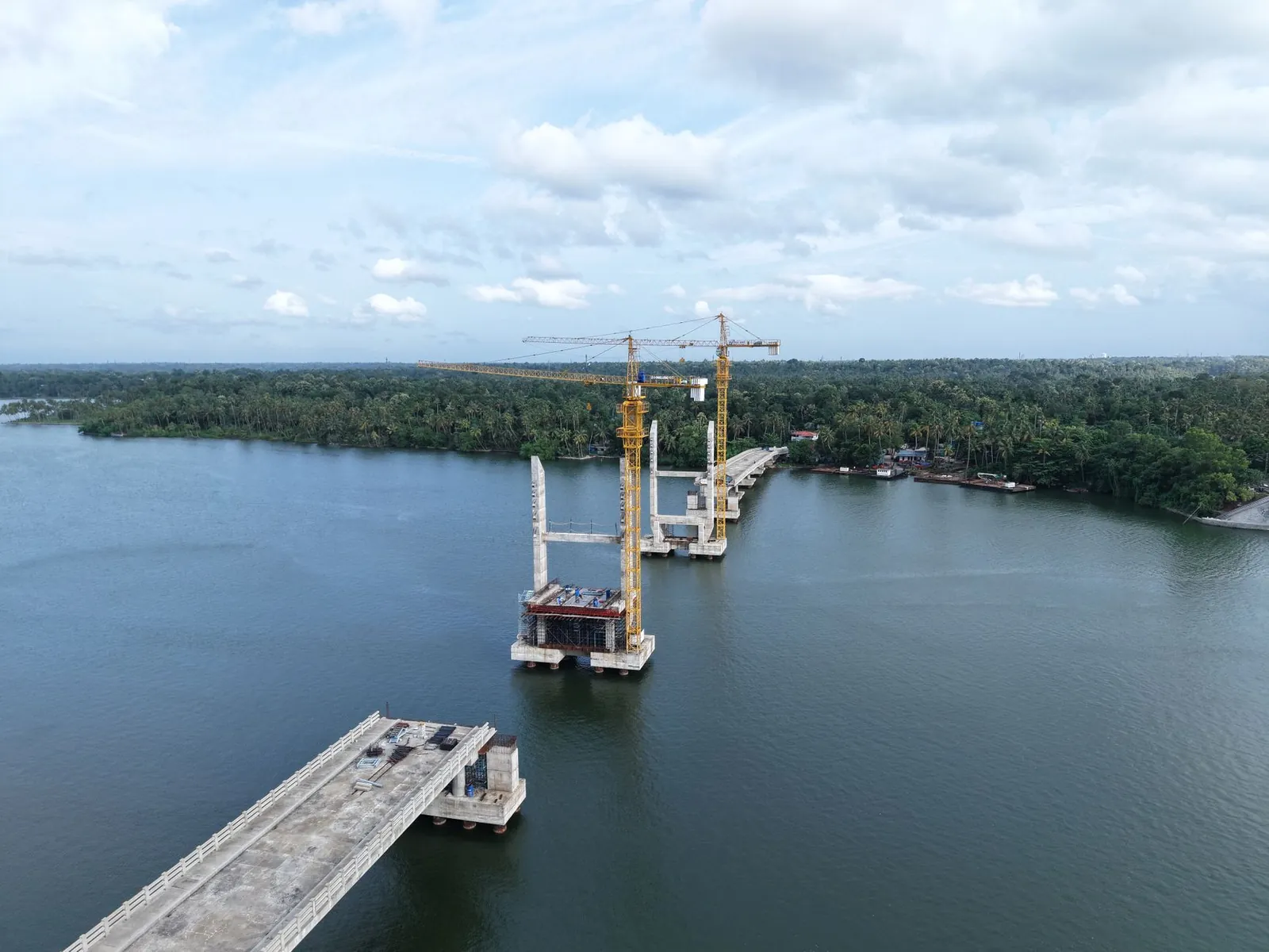 Aerial shot of a bridge under construction over a river in Kerala, India with cranes and lush greenery. Stock photo illustrating Brahmaputra Infrastructure's new order story.
