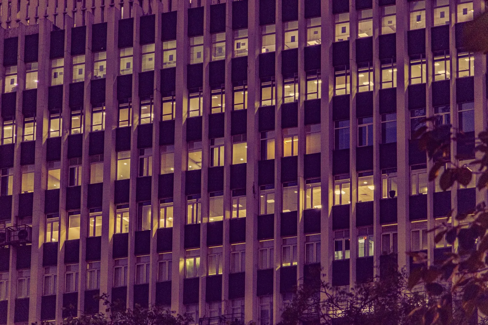 Illuminated urban office building facade at night in New Delhi, showcasing modern architecture with glowing windows. Stock photo illustrating Vibrant Global Capital's regulatory approval story.