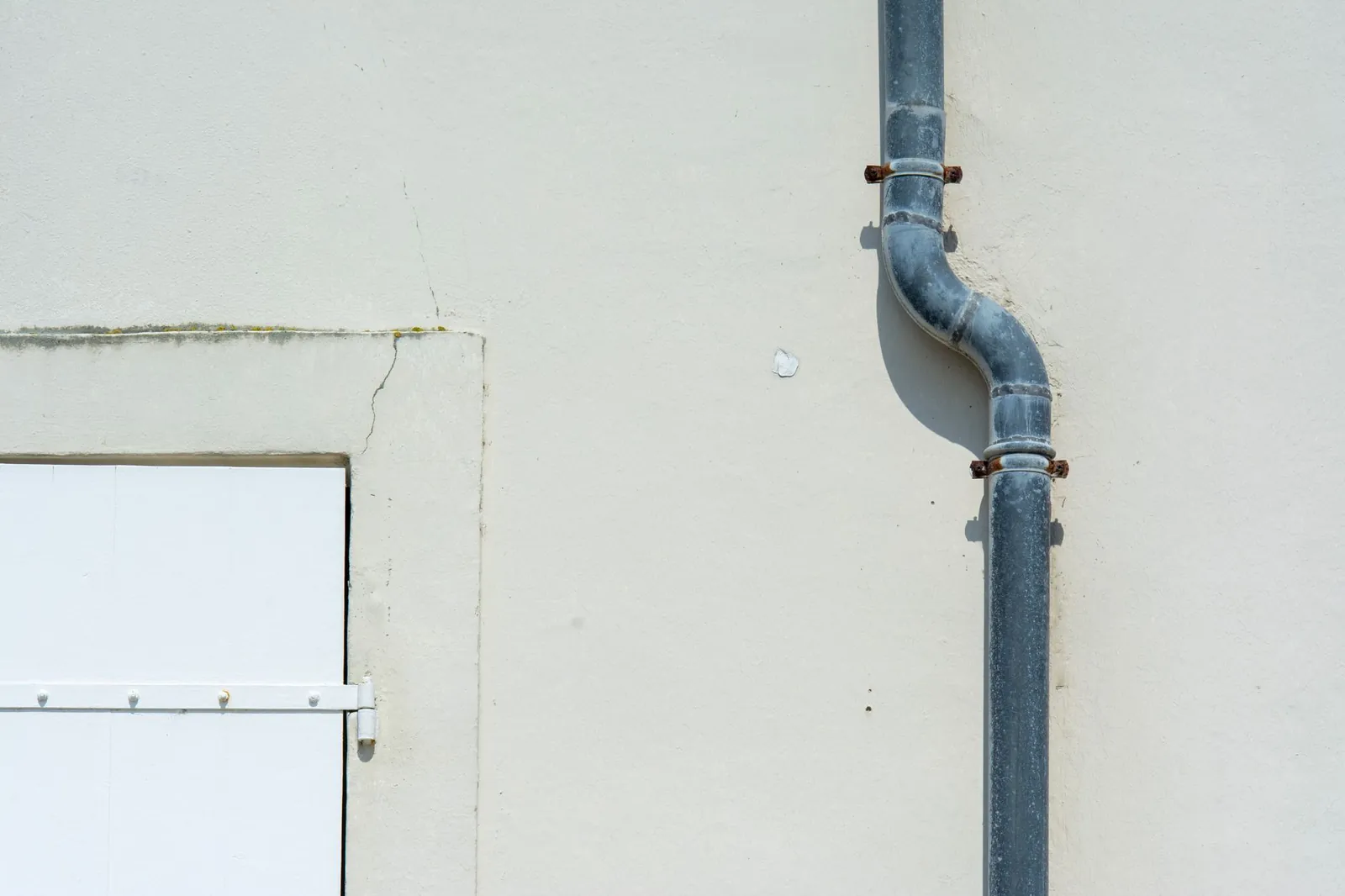 Close-up of a gray metal drainpipe attached to a plain exterior wall. Stock photo illustrating EMS's new order story.