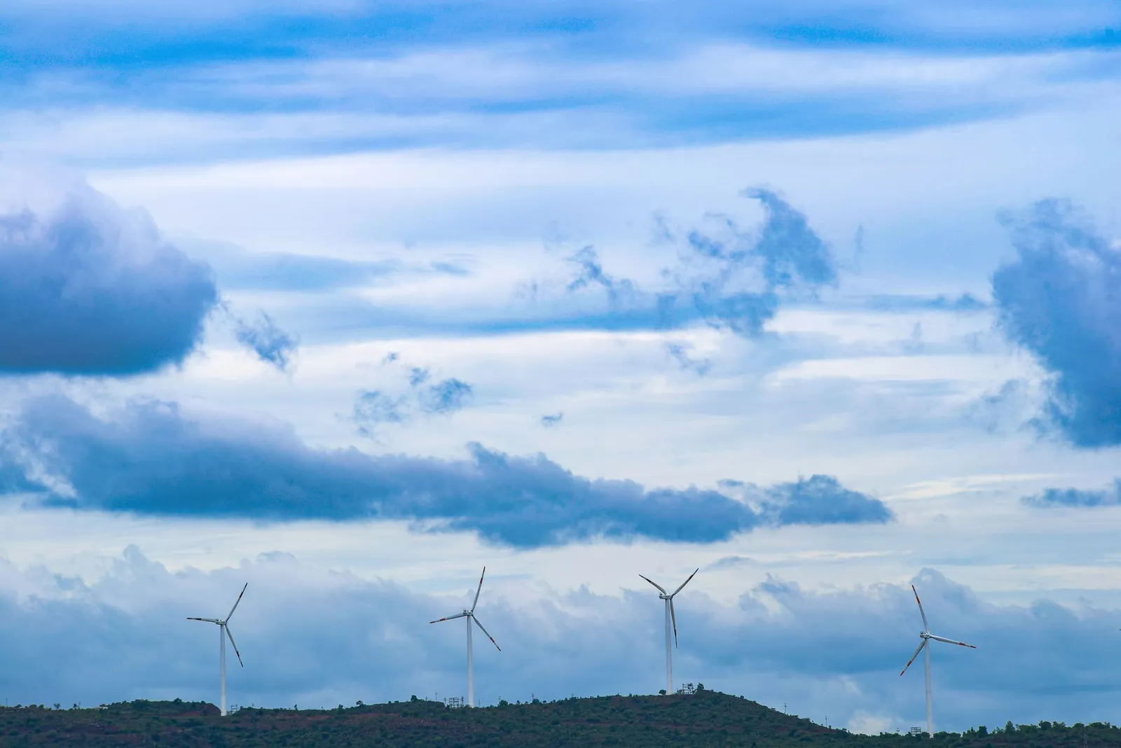 Wind turbines on a hill under a blue sky and scattered clouds, promoting renewable energy. Stock photo illustrating Inox Wind's new order story.