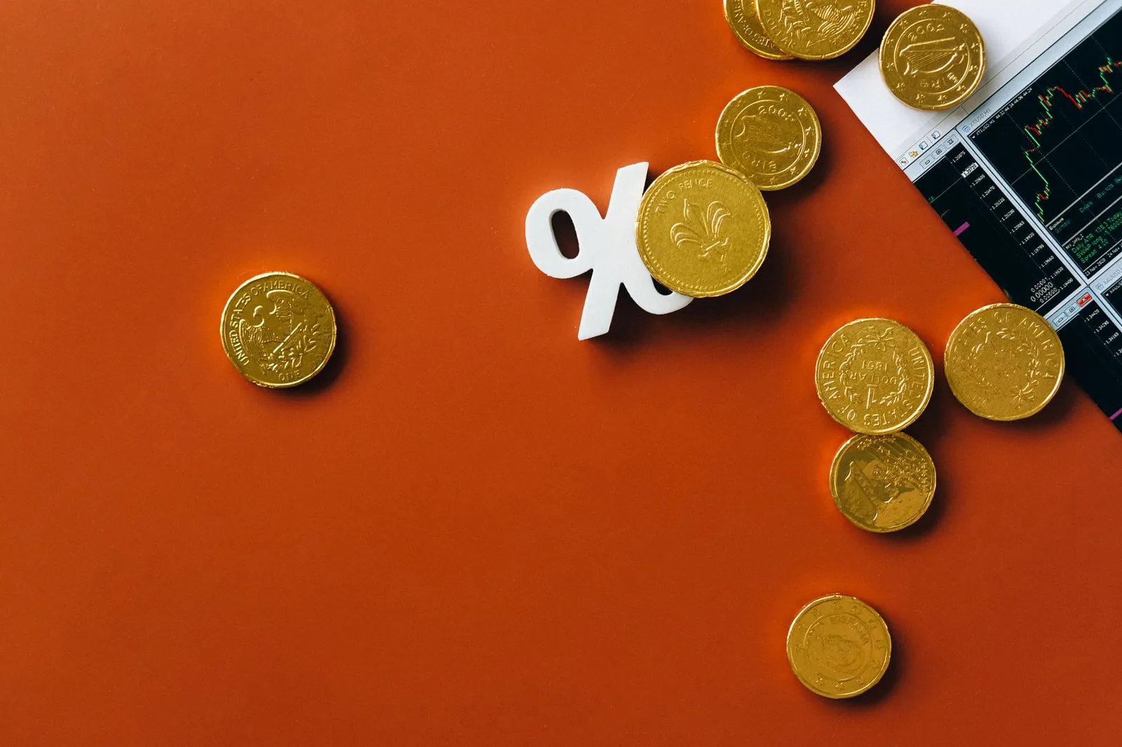 Gold coins scattered with a stock market graph and a percentage symbol on an orange background. Stock photo illustrating Augmont Enterprises' partnership story.