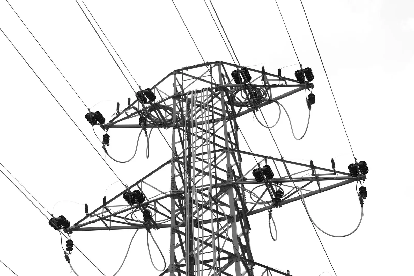 Black and white photo of high voltage power lines and electrical tower against a clear sky. Stock photo illustrating Transrail Lighting's fund raise story.
