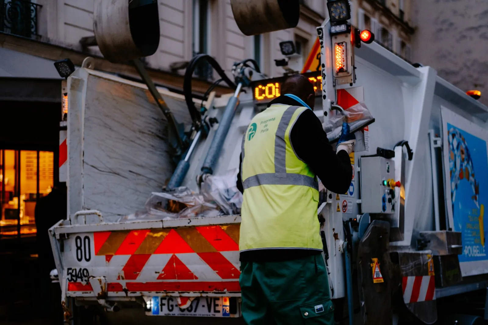 A garbage collector works on a city street, managing waste collection at dusk. Stock photo illustrating Urban Enviro Waste Management's fund raise story.