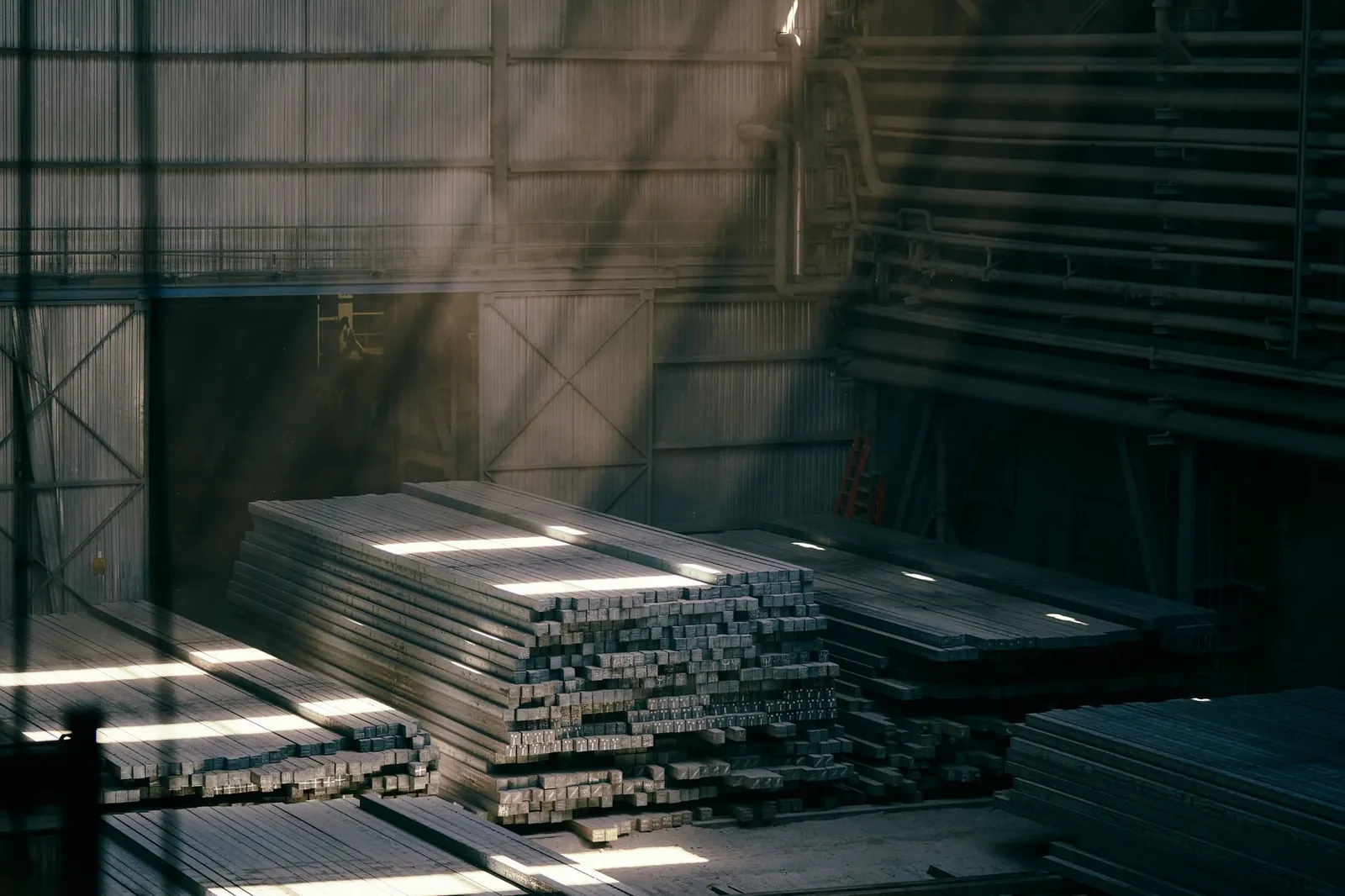 Sunlight streams into an industrial warehouse illuminating stacked steel beams. Stock photo illustrating Shyam Metalics and Energy's expansion story.