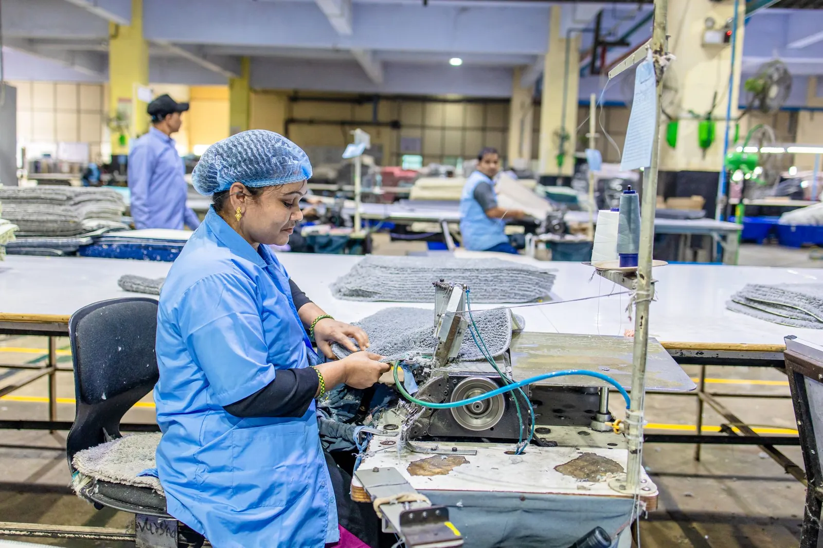 A female worker in a factory setting using a sewing machine for textile production. Stock photo illustrating Deepa Jewellers' earning call story.
