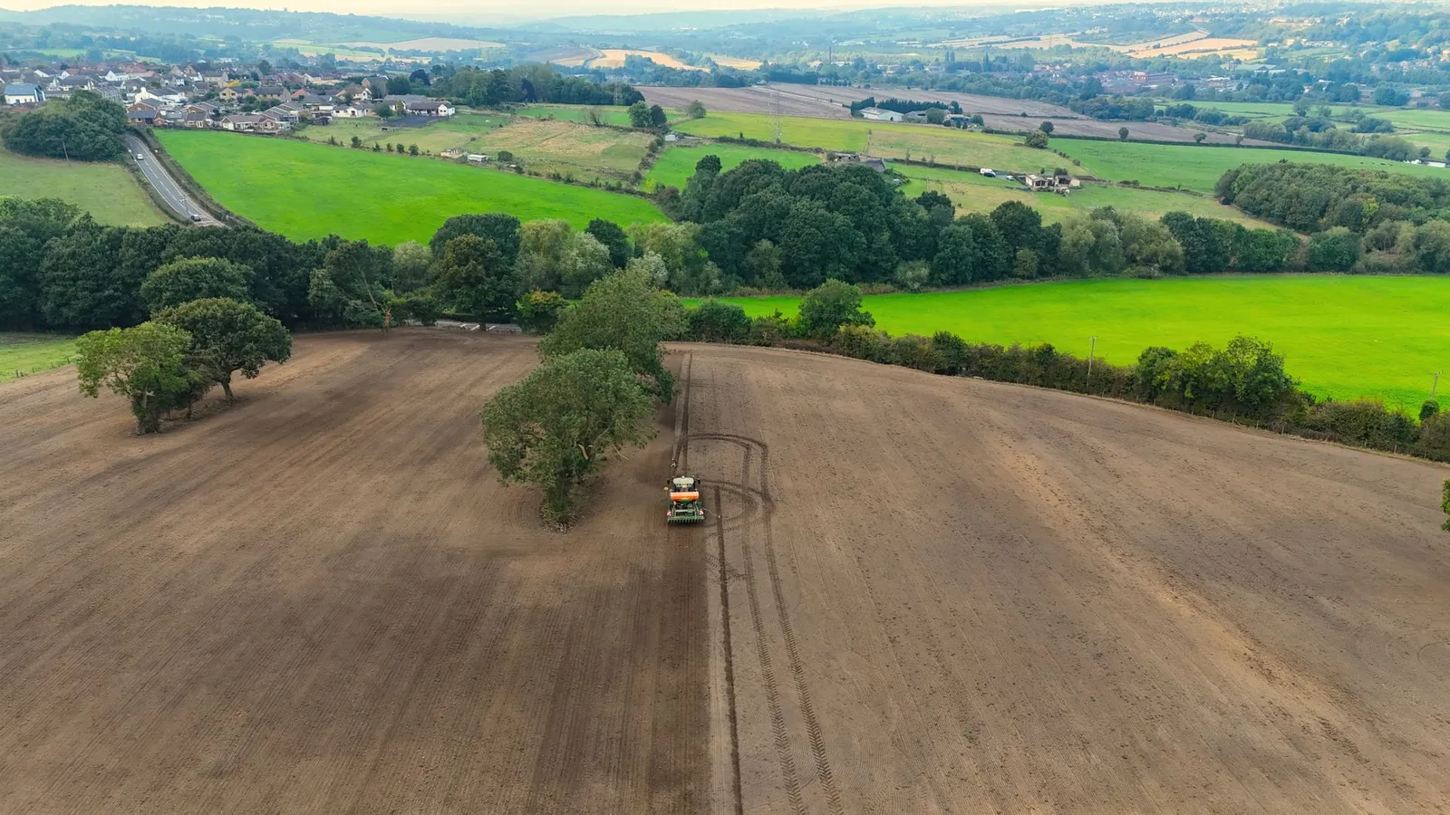 Aerial view of a tractor preparing fields near Wakefield, surrounded by lush greenery. Stock photo illustrating Bikewo Green Tech's new order story.