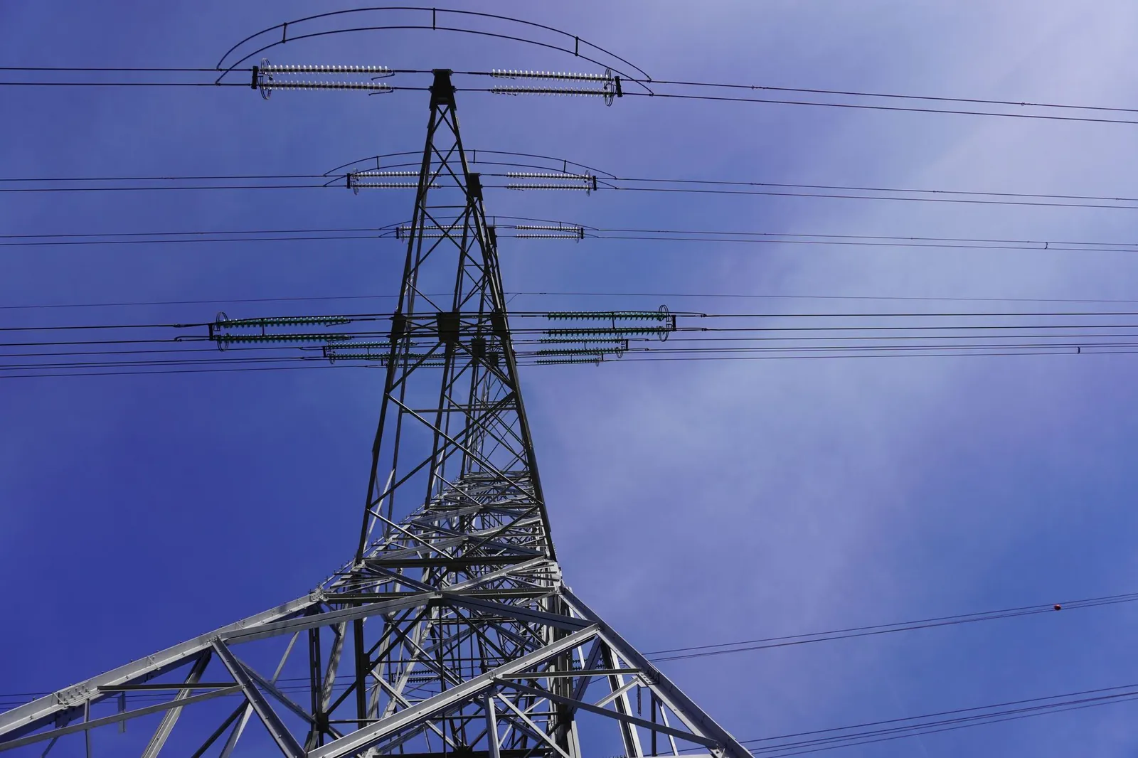 Steel electricity transmission tower against a clear blue sky, photographed from below. Stock photo illustrating Transrail Lighting's earning call story.