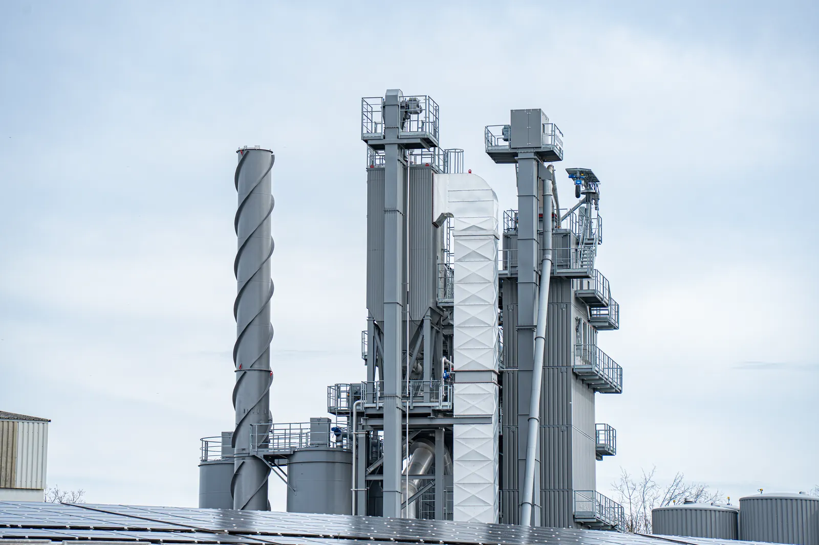 Gray industrial chimneys rise above factory buildings against a clear sky, showcasing modern industry. Stock photo illustrating Belrise Industries' fund raise story.