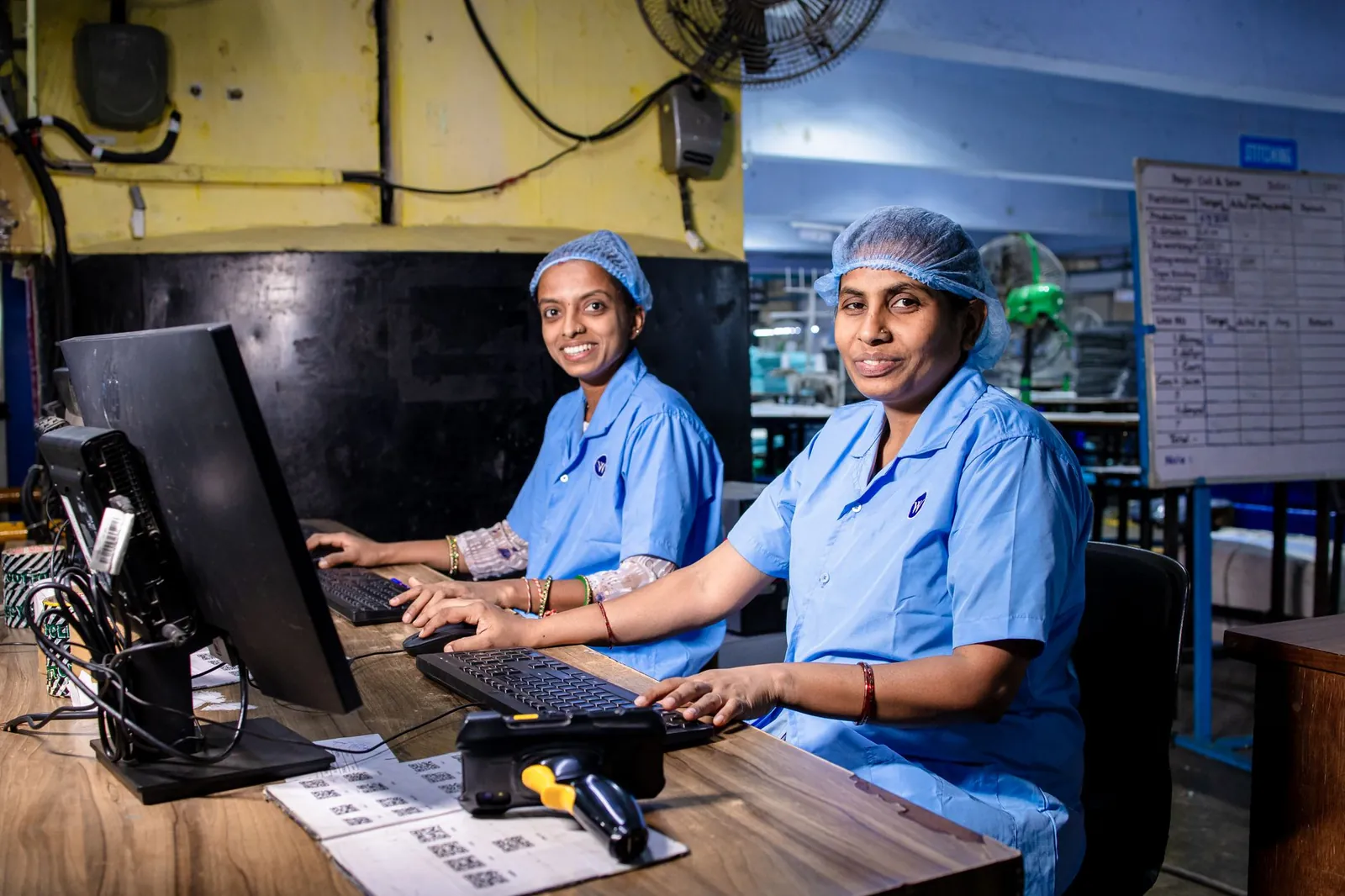 Two female workers at a textile factory operating computers in an industrial setting. Stock photo illustrating Optiemus Infracom's earning call story.