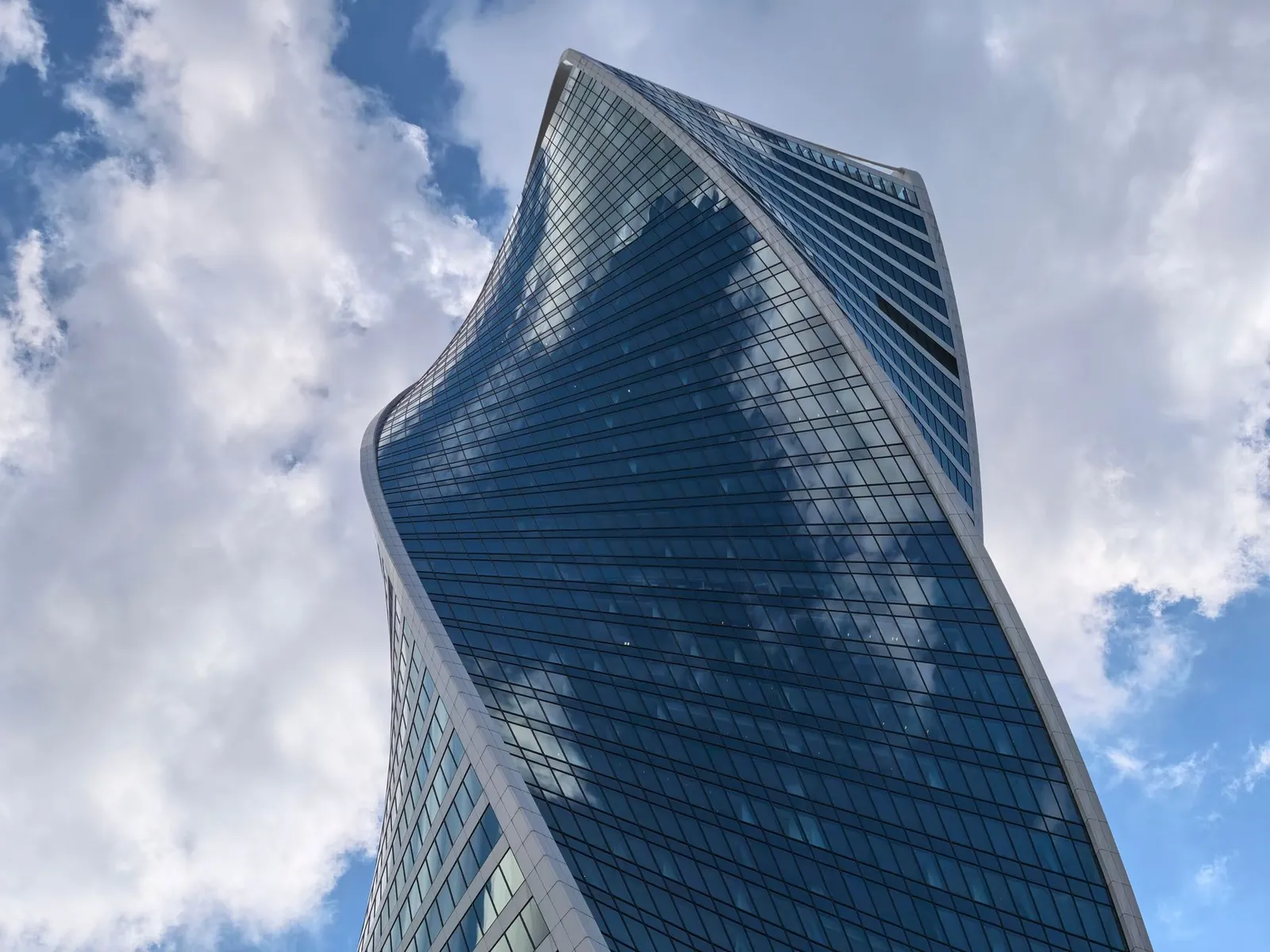 A modern twisting skyscraper with reflective glass under a bright, cloudy sky. Stock photo illustrating Garuda Construction and Engineering's partnership story.