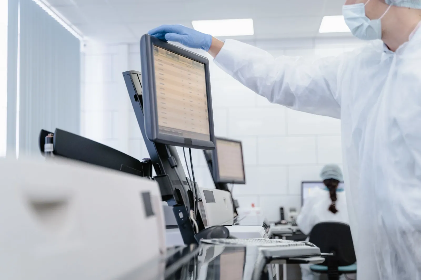Researcher in PPE reviews data on a digital screen in a modern laboratory setting. Stock photo illustrating Infosys' partnership story.