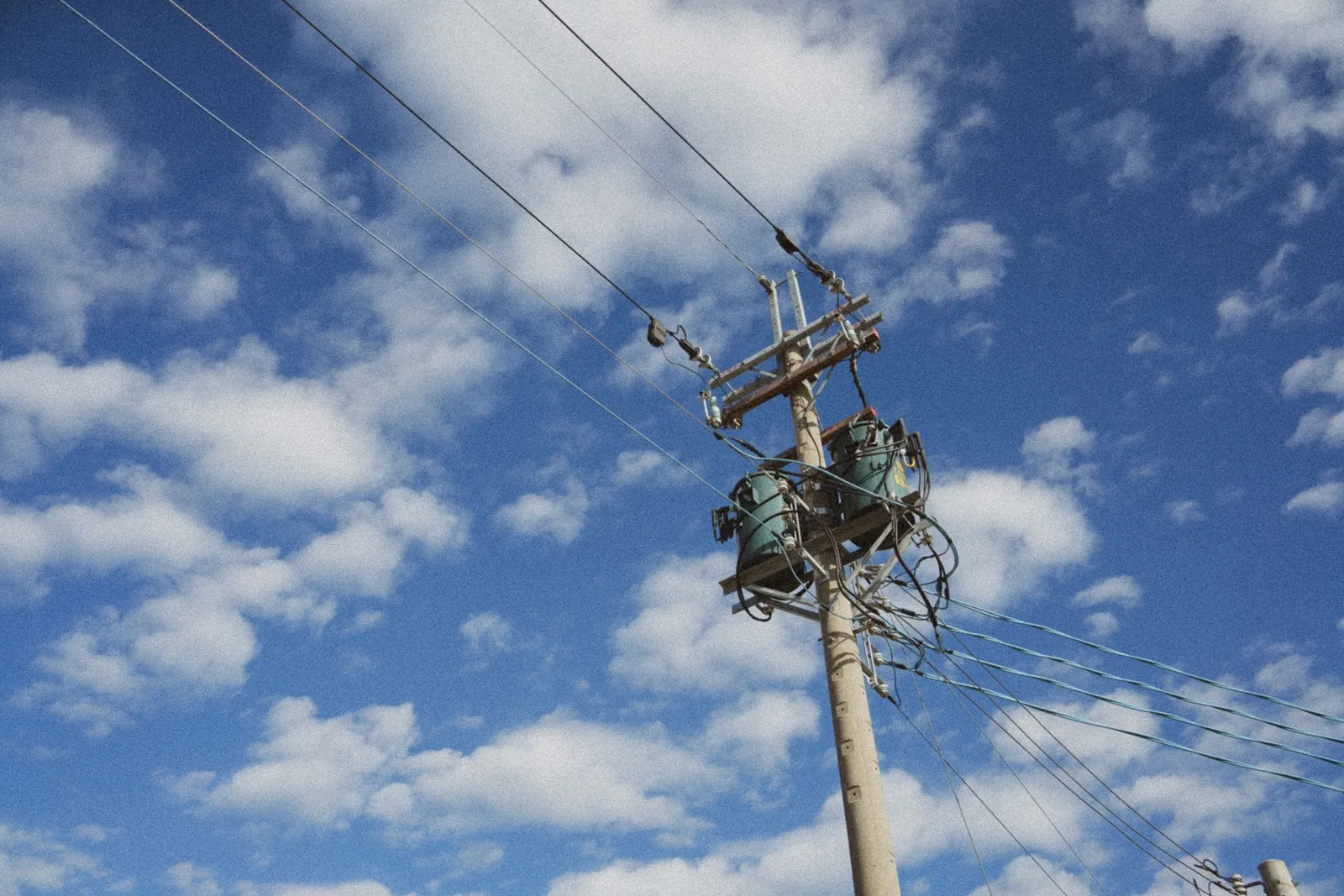 High voltage power lines stretching against a cloud-dappled blue sky, showcasing modern energy infrastructure. Stock photo illustrating Yash Highvoltage's production started story.