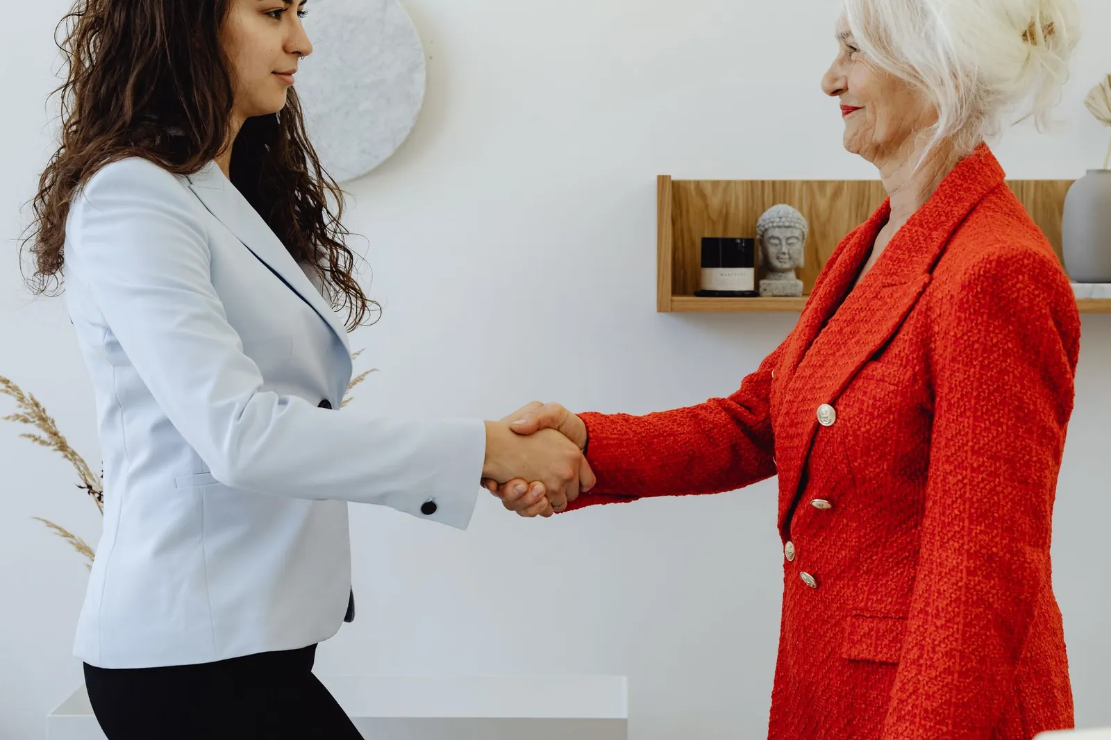 Two professional women elegantly shaking hands in a modern office setting, symbolizing agreement and leadership. Stock photo illustrating Aavas Financiers' regulatory approval story.