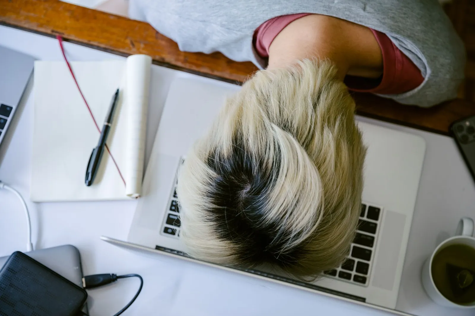 From above of tired fatigued unrecognizable female in casual wear resting head on netbook keyboard near notebook and cup of tea after long working day. Stock photo for the ALFA News guide: How to Avoid Alert Fatigue in Trading.