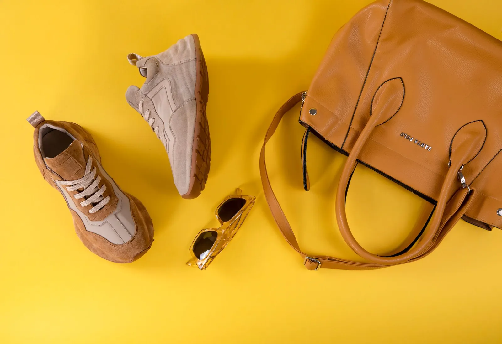Stylish brown handbag, fashionable eyewear, and sport shoes on vibrant yellow background. Stock photo illustrating Lehar Footwears' earning call story.