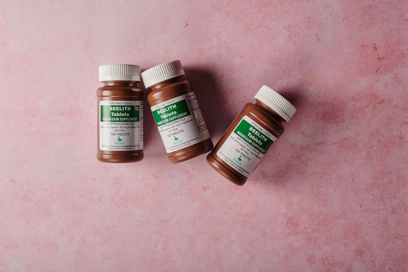 Three brown bottles of magnesium tablets on a soft pink background, ideal for health-themed content. Stock photo illustrating Aayush Wellness' product launched story.