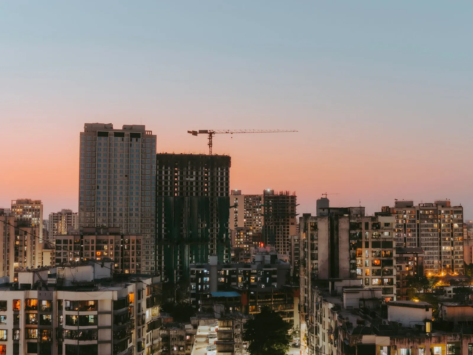 Cityscape view with buildings and a construction crane at sunset, highlighting urban development. Stock photo illustrating Arkade Developers' expansion story.