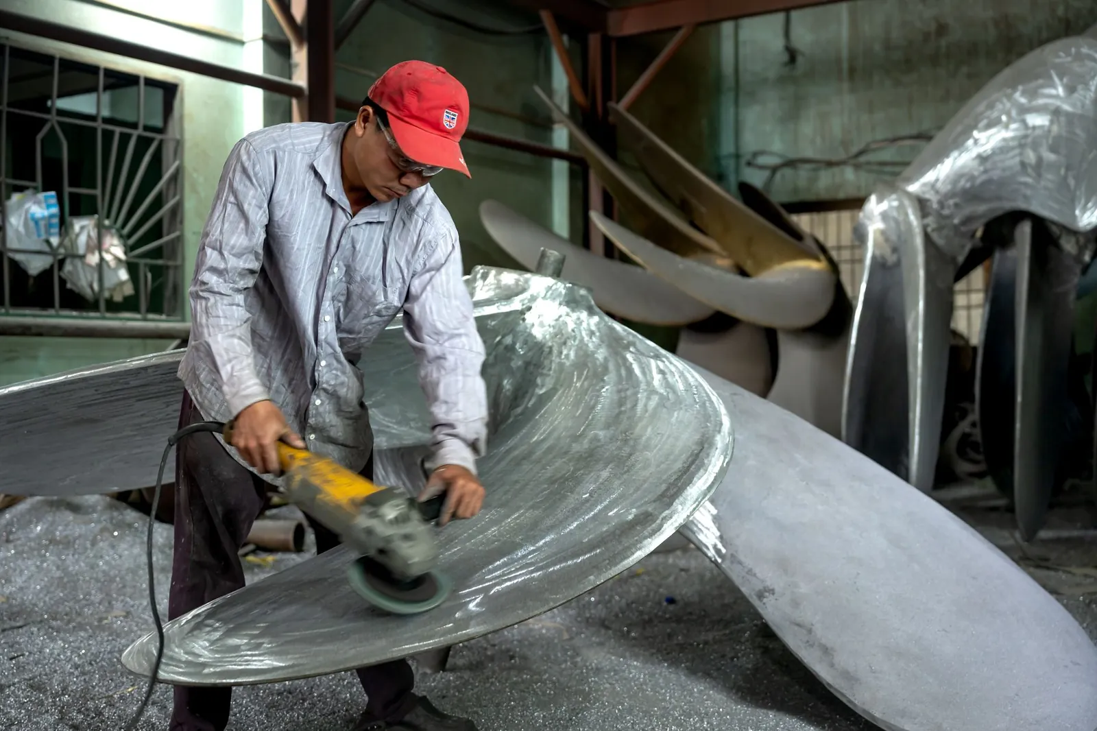 Worker in a workshop grinding a large metal propeller, showcasing industrial craftsmanship. Stock photo illustrating ACC's production started story.