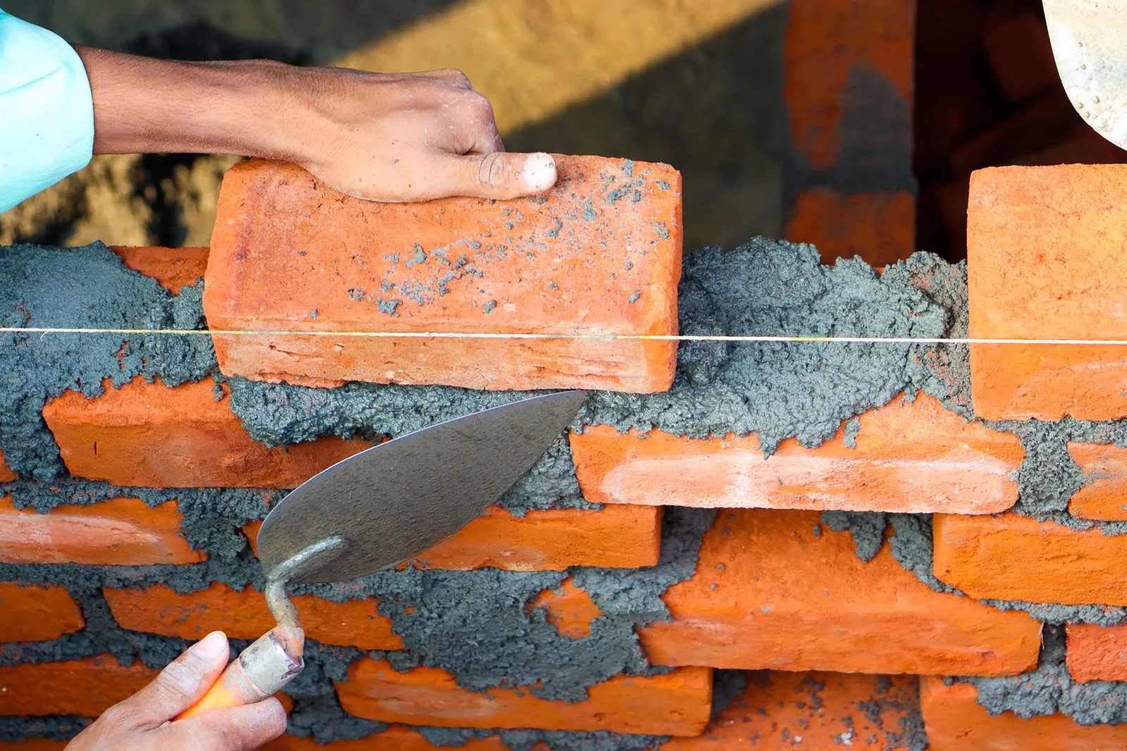 Hands laying bricks with cement in a construction setting, showcasing precise masonry work. Stock photo illustrating Manav Infra Projects' new order story.
