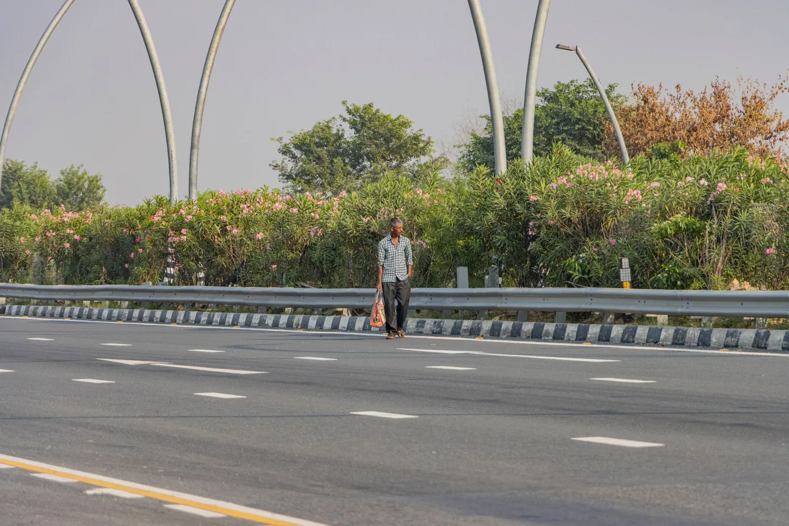 A man walking on a highway in Deeg, Uttar Pradesh, India, surrounded by lush greenery and flowers. Stock photo illustrating PNC Infratech's expansion story.