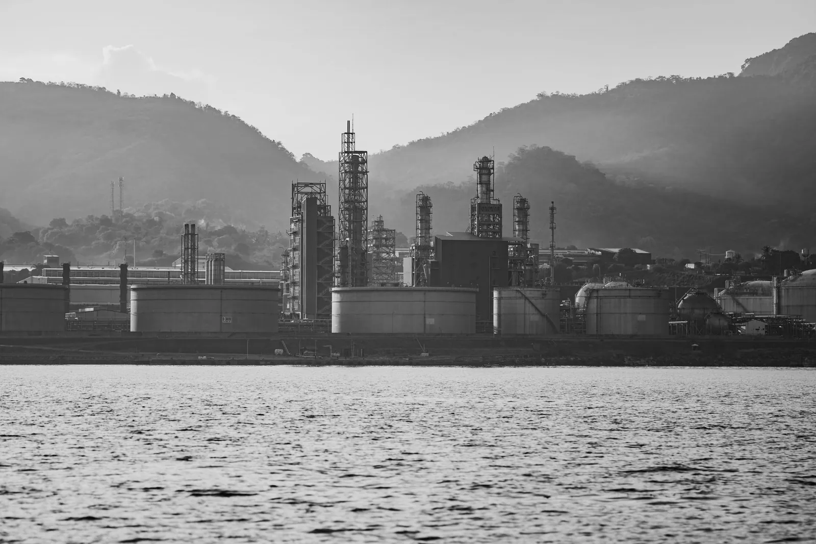 A monochrome shot of an industrial refinery near mountains, highlighting its structures. Stock photo illustrating Deepak Nitrite's financial results story.