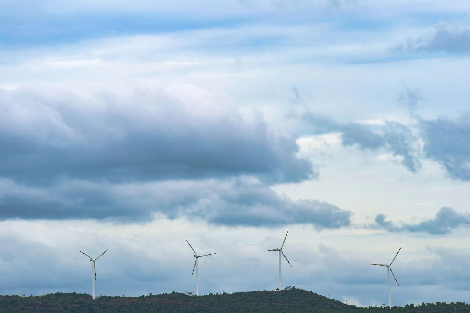 Scenic view of wind turbines on a hill with a cloudy sky, representing renewable energy. Stock photo illustrating K.P. Energy's new order story.