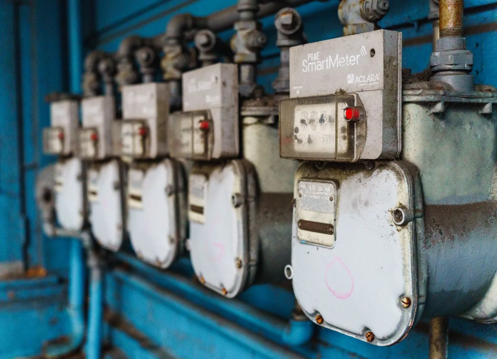 Multiple smart utility meters lined up on a blue industrial wall. Stock photo illustrating Valiant Communications' new order story.
