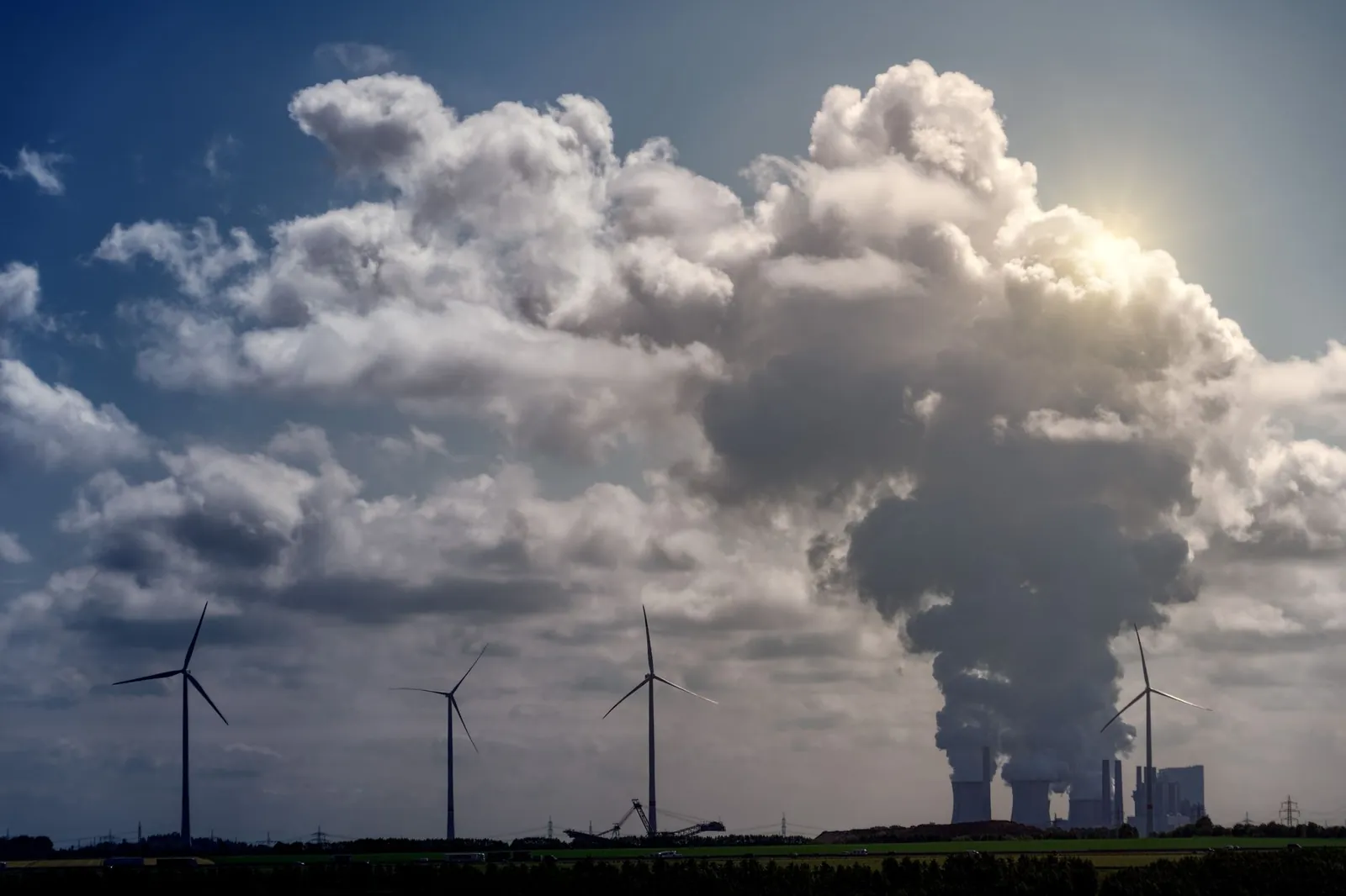 Wind turbines and a power plant under dramatic cumulus clouds in a rural landscape. Stock photo illustrating GE Power India's earning call story.