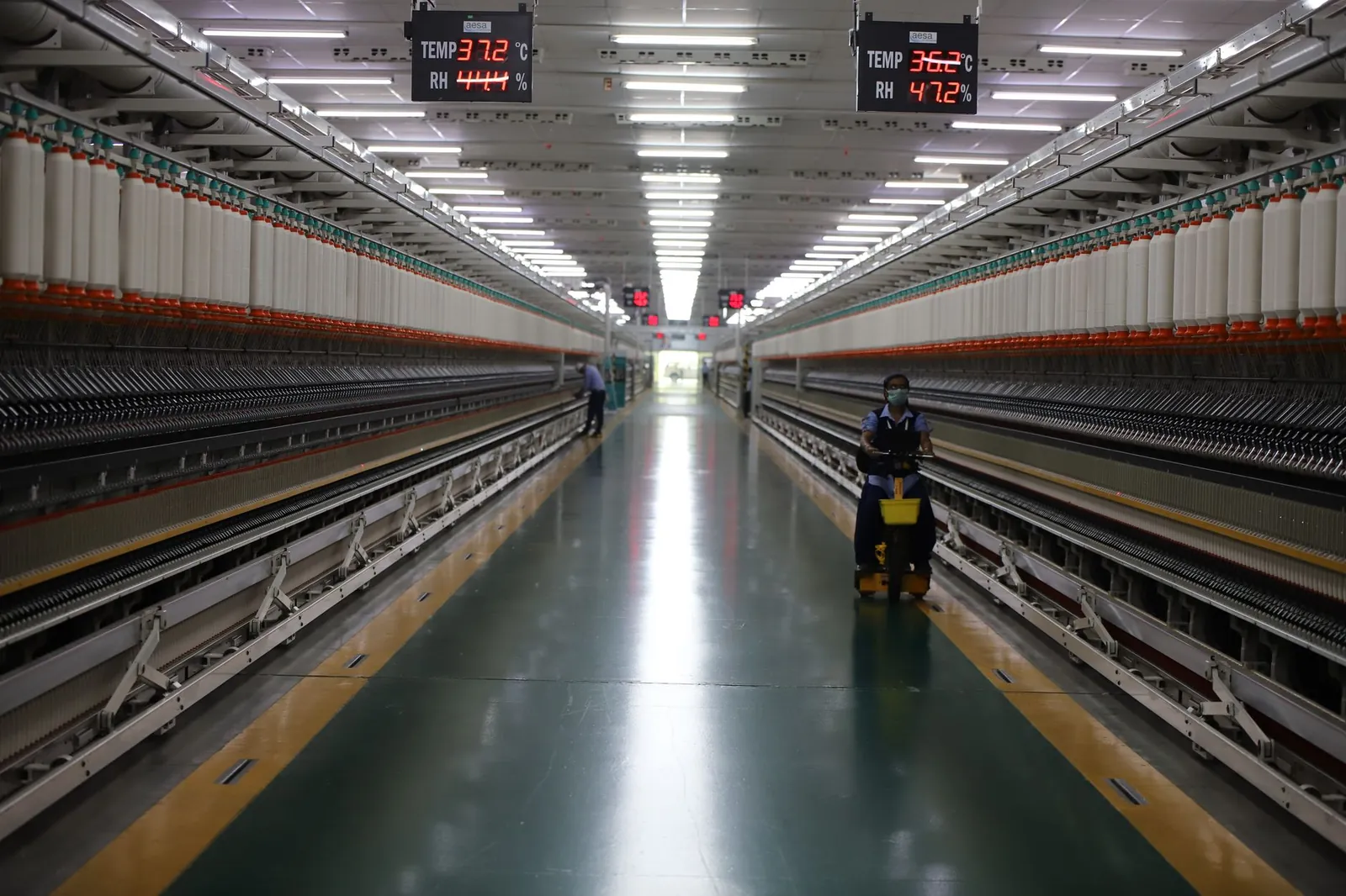Long hallway in Indian textile factory with spinning machinery and workers. Stock photo illustrating Super Sales India's financial results story.