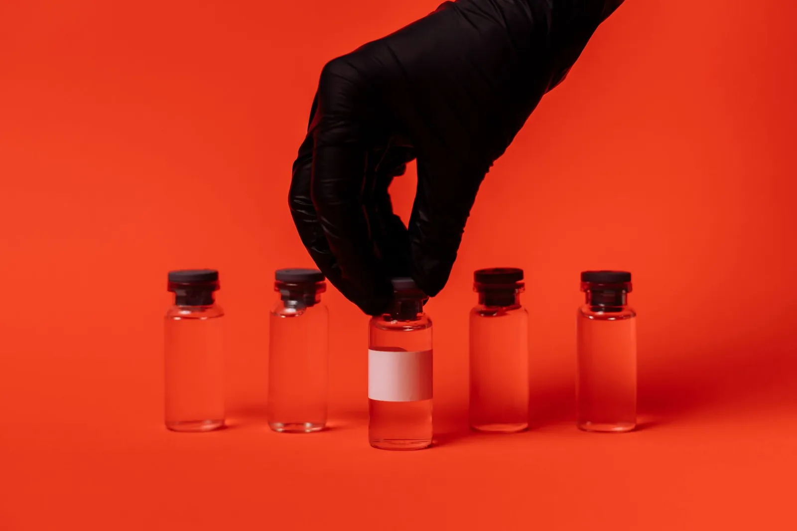 Person wearing black glove grabbing a vaccine vial against a bright red backdrop. Stock photo illustrating Dr Reddys Laboratories' partnership story.