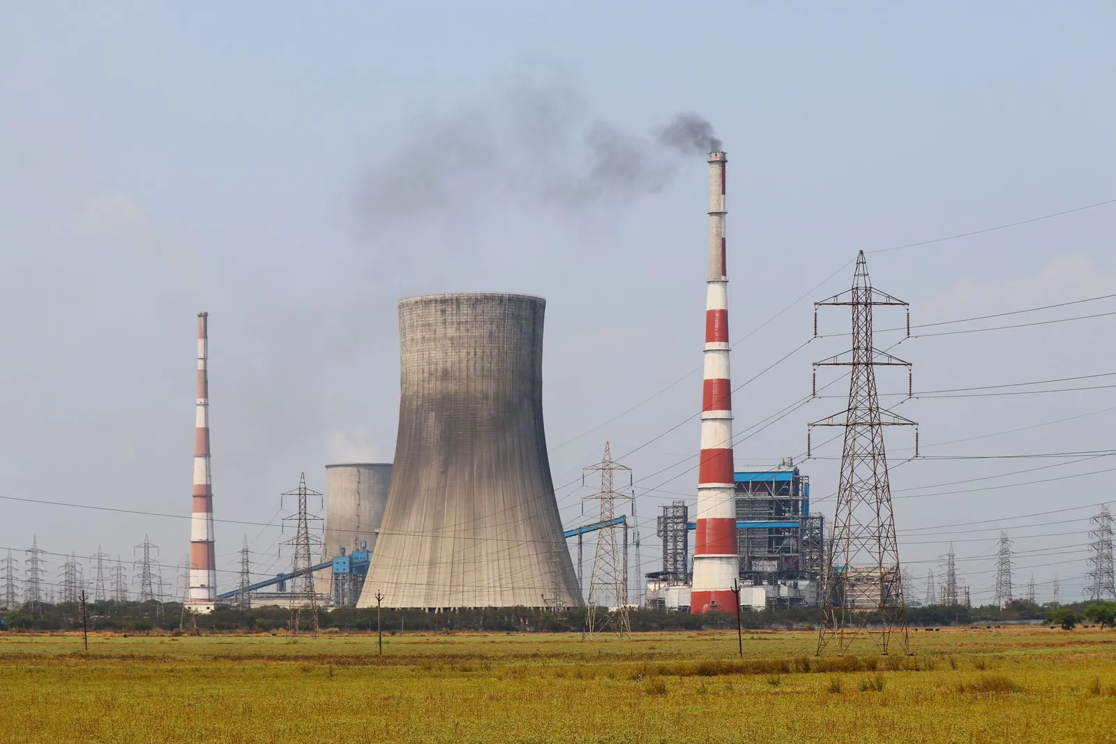 Smokestacks and a cooling tower emit smoke at a power plant in Vijayawada, India. Stock photo illustrating Power Mech Projects' new order story.