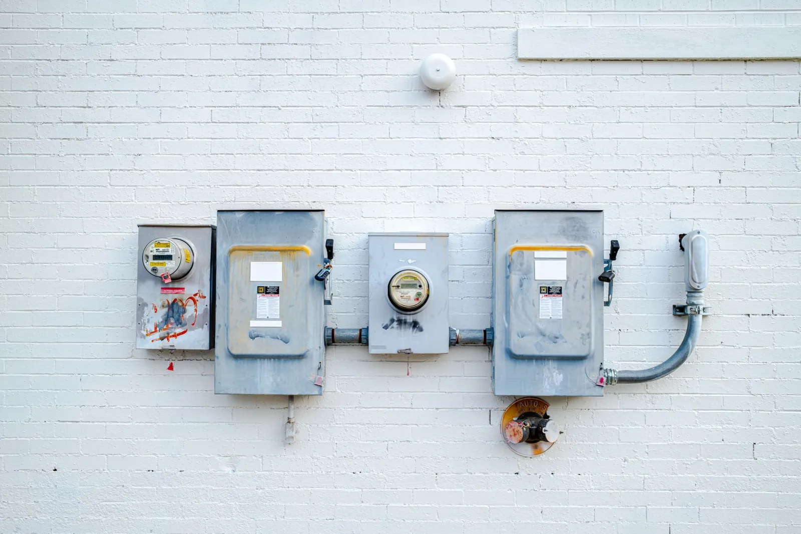 Electrical boxes and power meters mounted on a white brick wall. Stock photo illustrating RMC Switchgears' new order story.