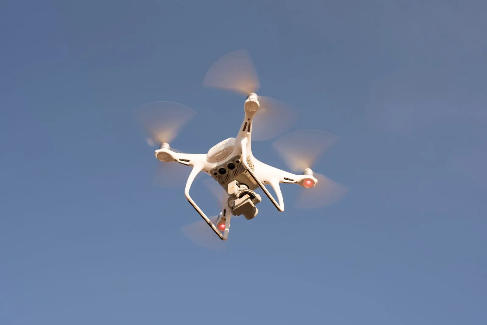 A white drone in flight against a clear blue sky, capturing aerial footage with precision. Stock photo illustrating Tembo Global Industries' production started story.