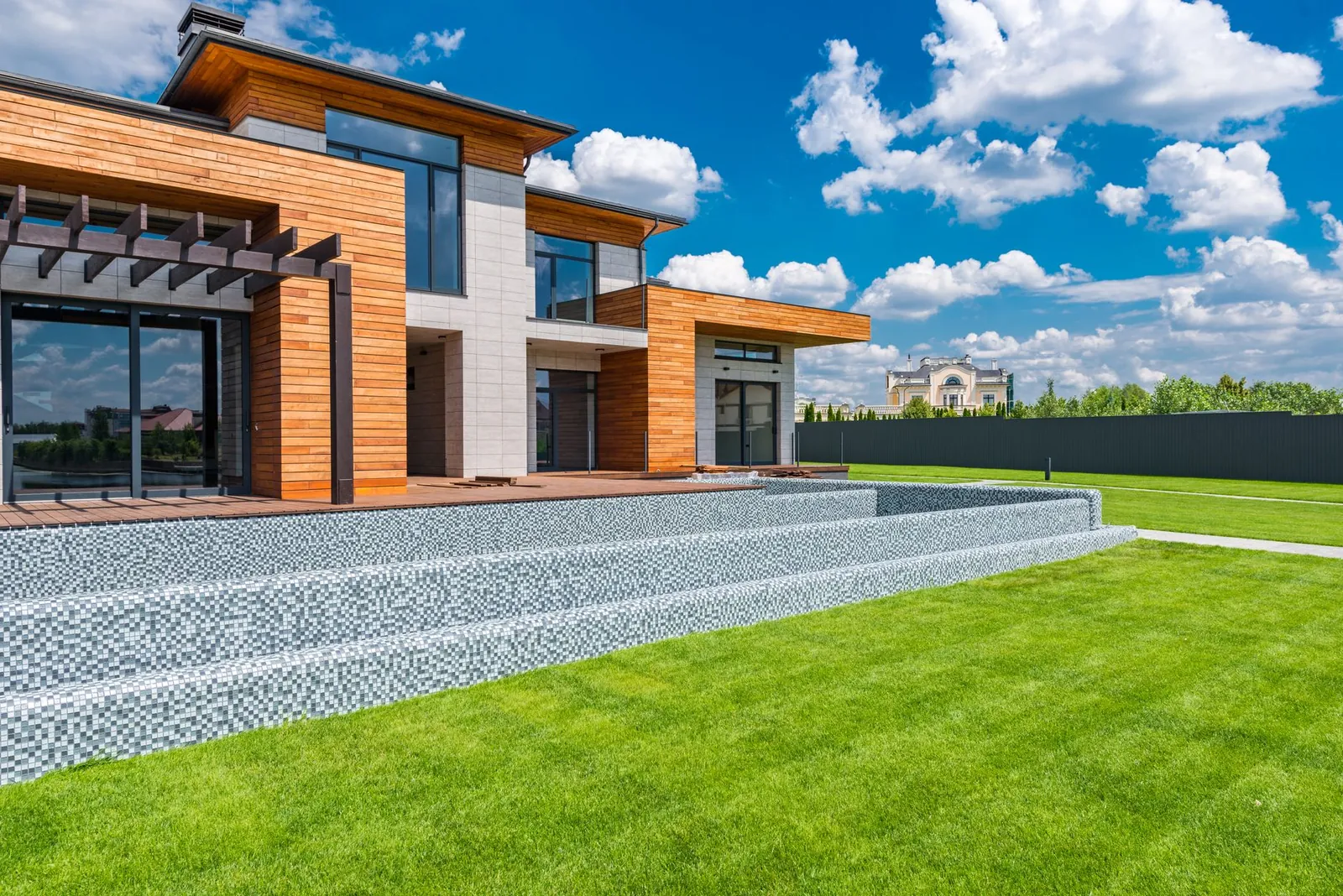 Exterior of contemporary residential house with panoramic windows glass doors and green lawn in yard on sunny day against blue sky with white clouds. Stock photo illustrating Hazoor Multi Projects' new order story.