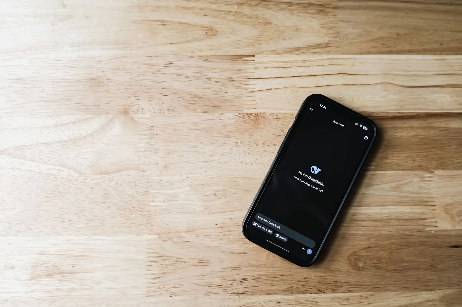 Top-down view of a smartphone displaying a chatbot interface on a light wooden surface. Stock photo illustrating Methodhub Software's product launched story.
