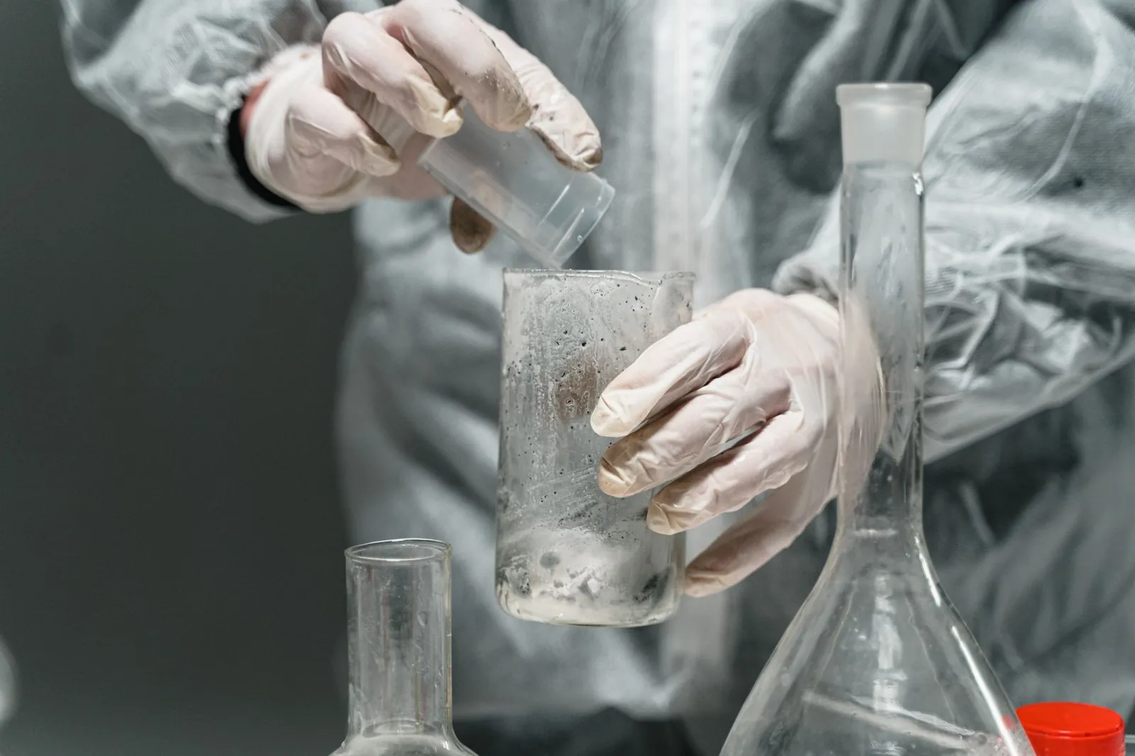 Scientist in a lab coat working with glassware and chemicals for research in a laboratory setting. Stock photo illustrating Aether Industries' production started story.