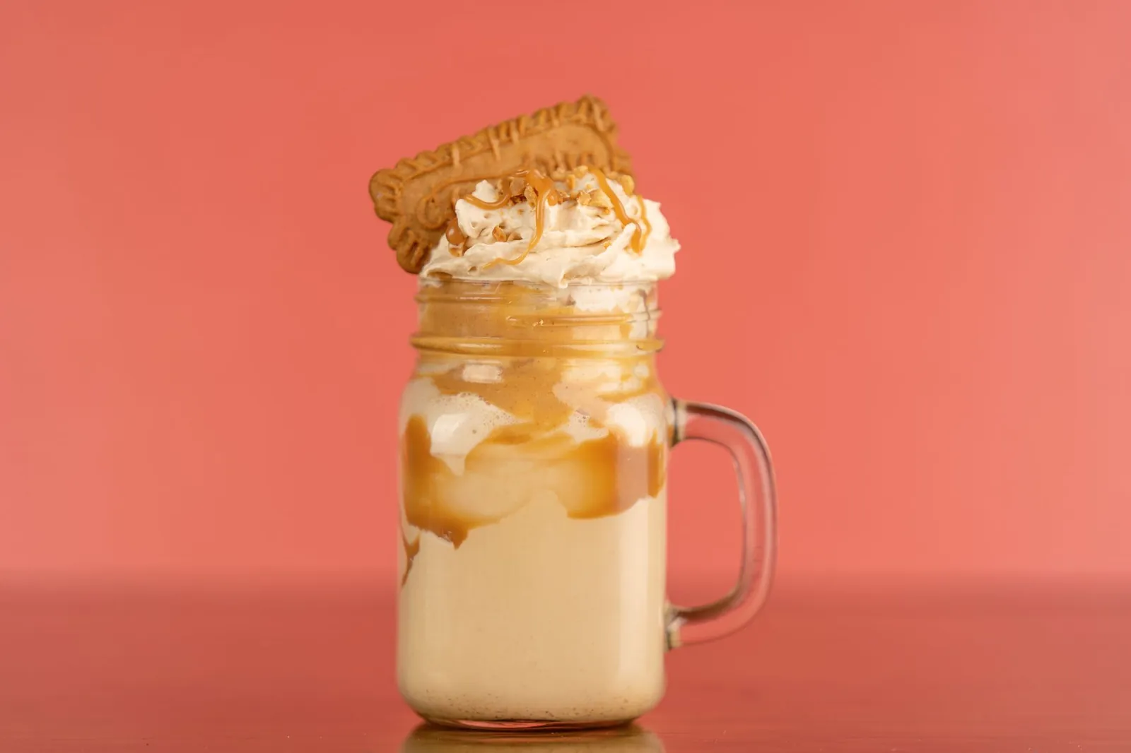 Close-up of a caramel milkshake with whipped cream and biscuit topping against a salmon background. Stock photo illustrating Heritage Foods' product launched story.