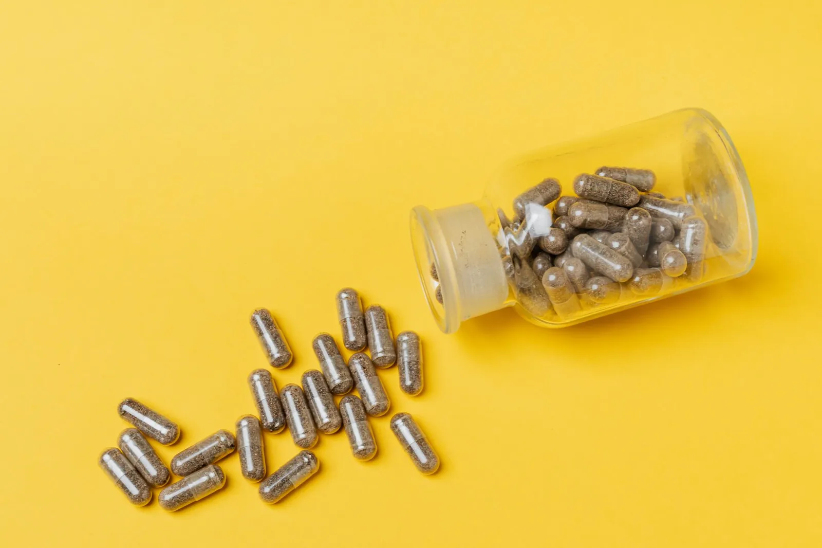 A glass bottle spilling capsules on a vivid yellow background. Perfect for healthcare and medicine themes. Stock photo illustrating Jeena Sikho Lifecare's product launched story.