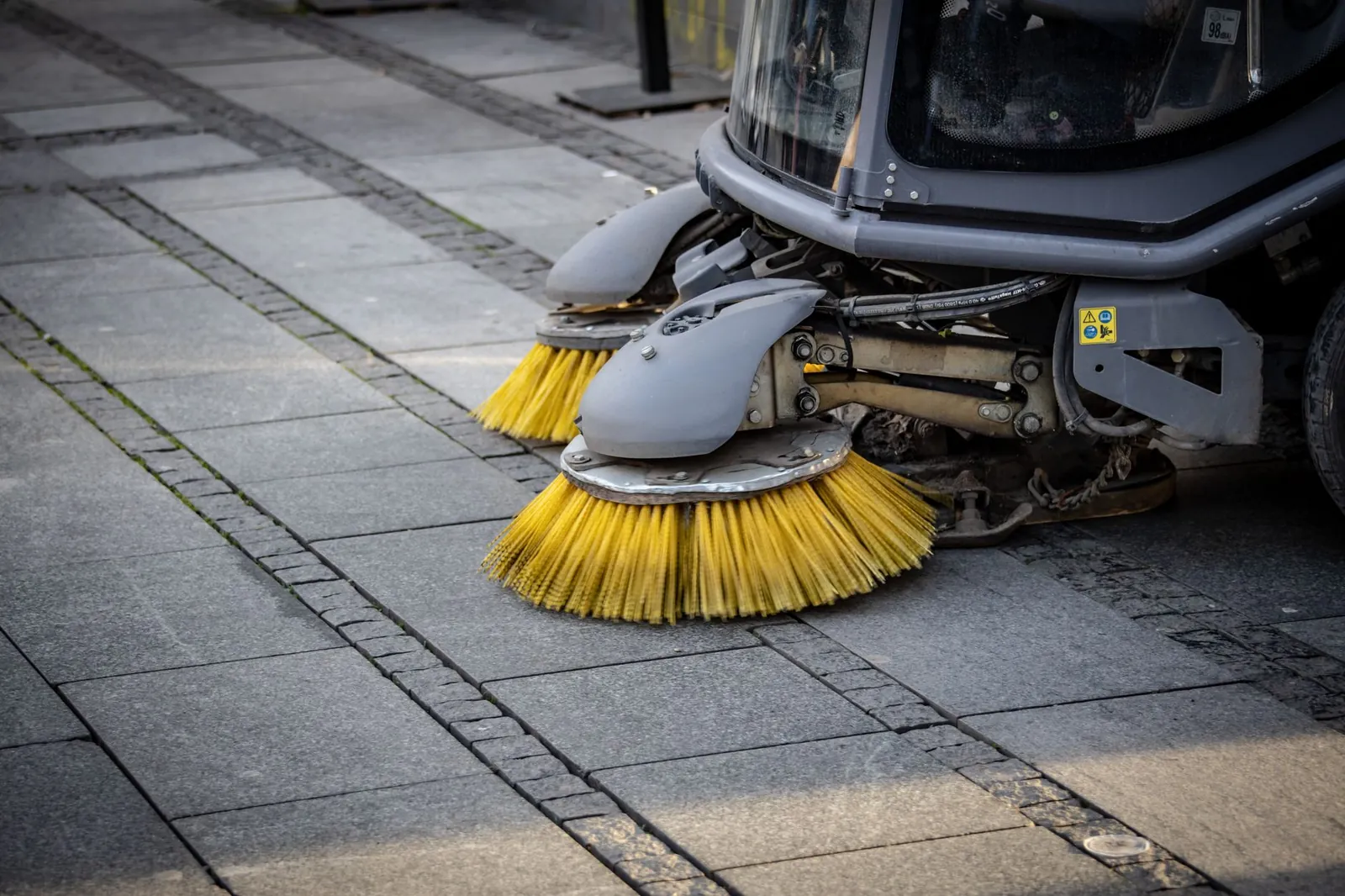 Close-up view of a road sweeper's yellow brushes on a paved street. Stock photo illustrating Antony Waste Handling Cell's new order story.