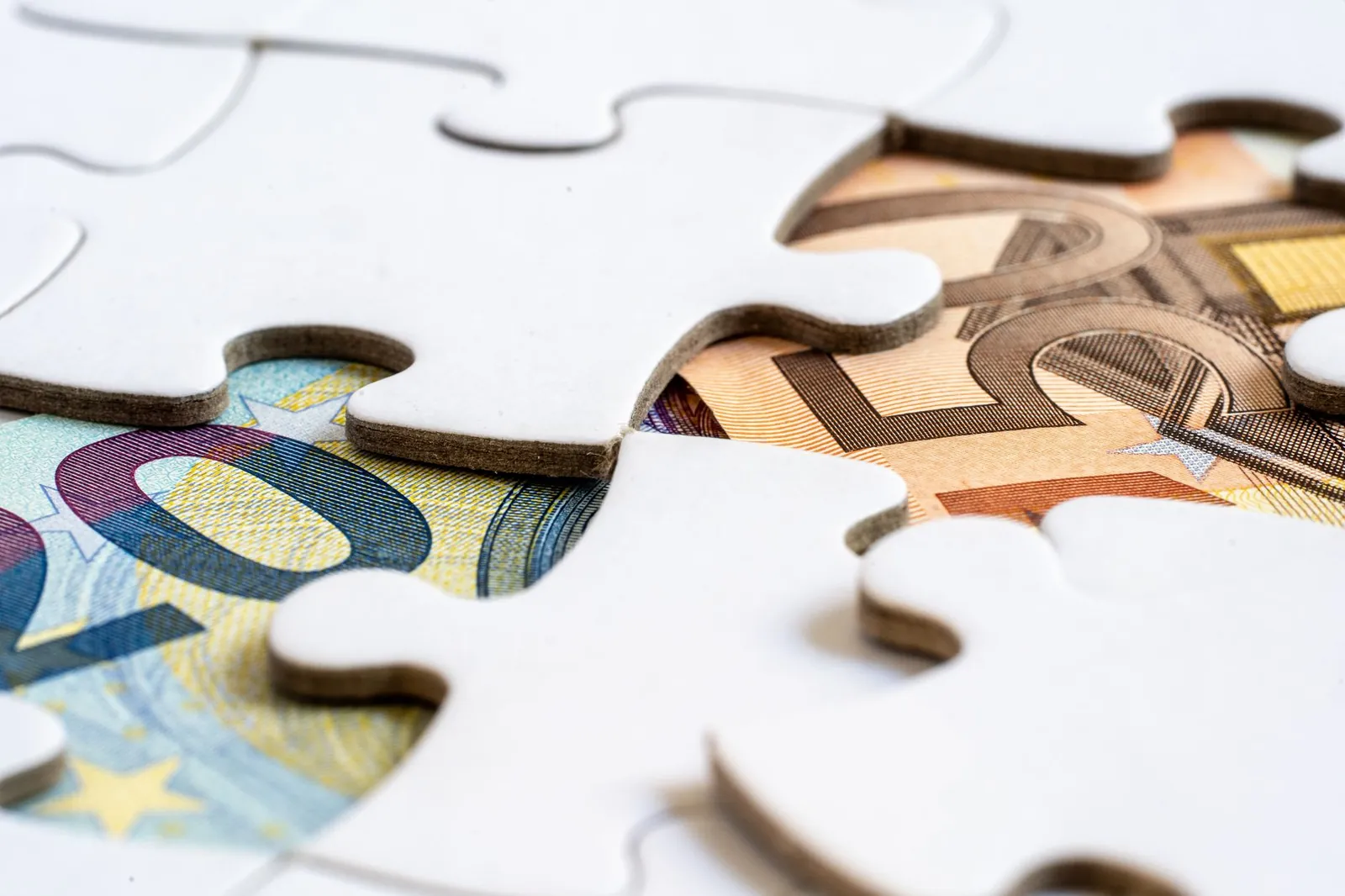 Close-up of euro banknotes revealed under puzzle pieces, symbolizing financial solutions. Stock photo for the ALFA News guide: Disclosure Under Regulation 30: A SEBI LODR Guide.