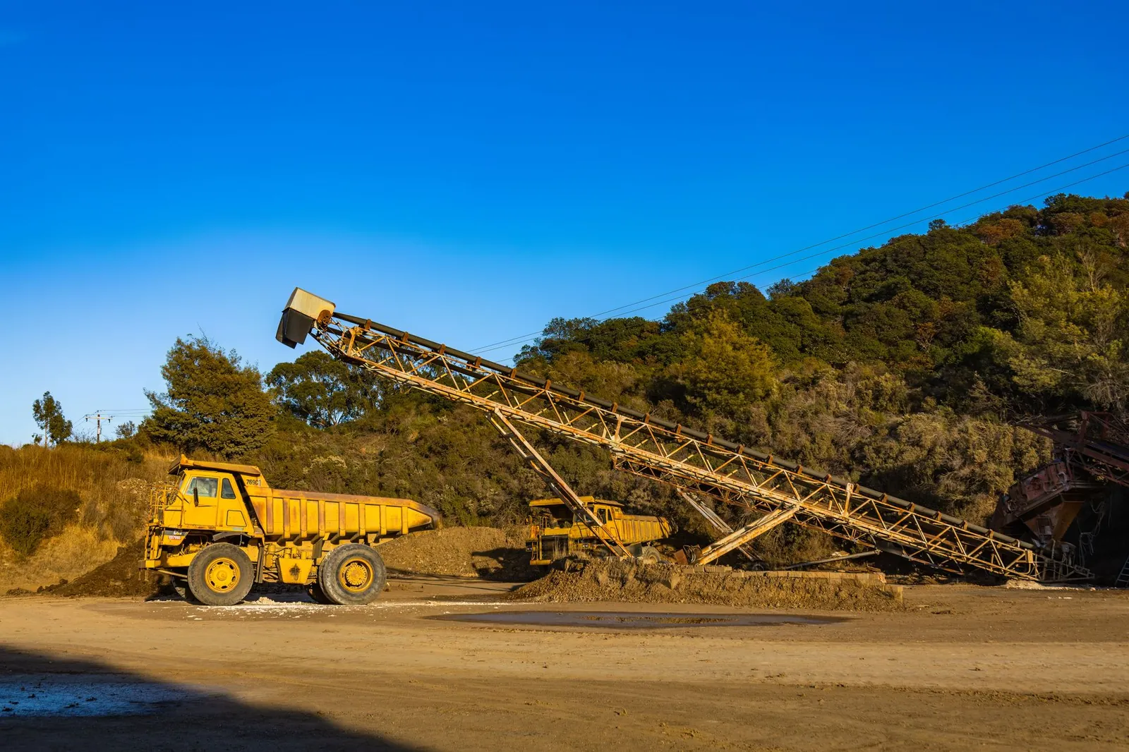 Yellow dump trucks and conveyor machinery in a sunny mining site with clear blue sky. Stock photo illustrating Kalind's new order story.