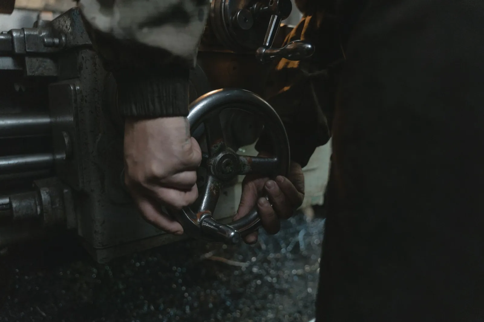 Close-up of hands operating a lathe machine in a workshop, showcasing precision metalwork. Stock photo illustrating Goodluck India's expansion story.