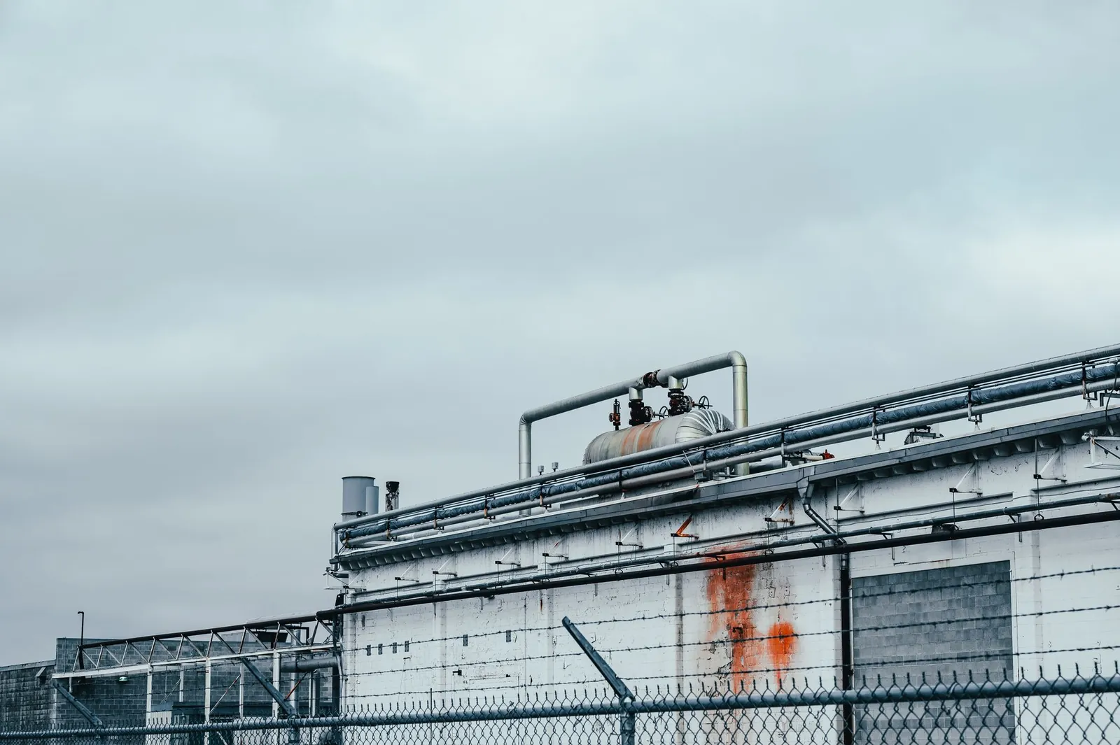 Shabby wall of factory with metal pipes and special equipment located near fence in industrial district of town against cloudy sky. Stock photo illustrating Manbro Industries' new order story.