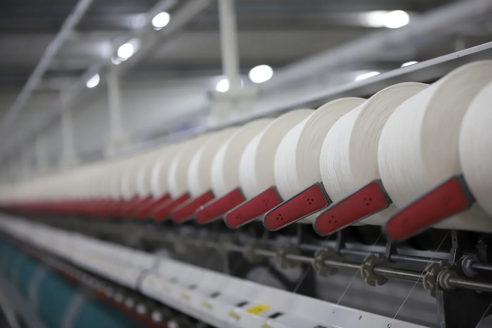 Close-up view of a textile production line showcasing white thread spools in an Indian factory. Stock photo illustrating Sportking India's financial results story.