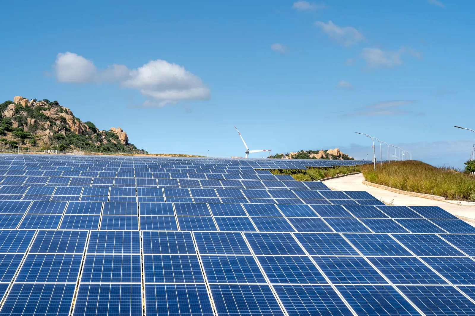 Expansive solar farm with rows of panels under clear blue sky and hills in the background. Stock photo illustrating Waaree Energies' new order story.